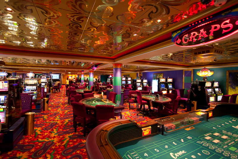 Interior of a carefully designed casino featuring craps and blackjack tables plus many slot machines.