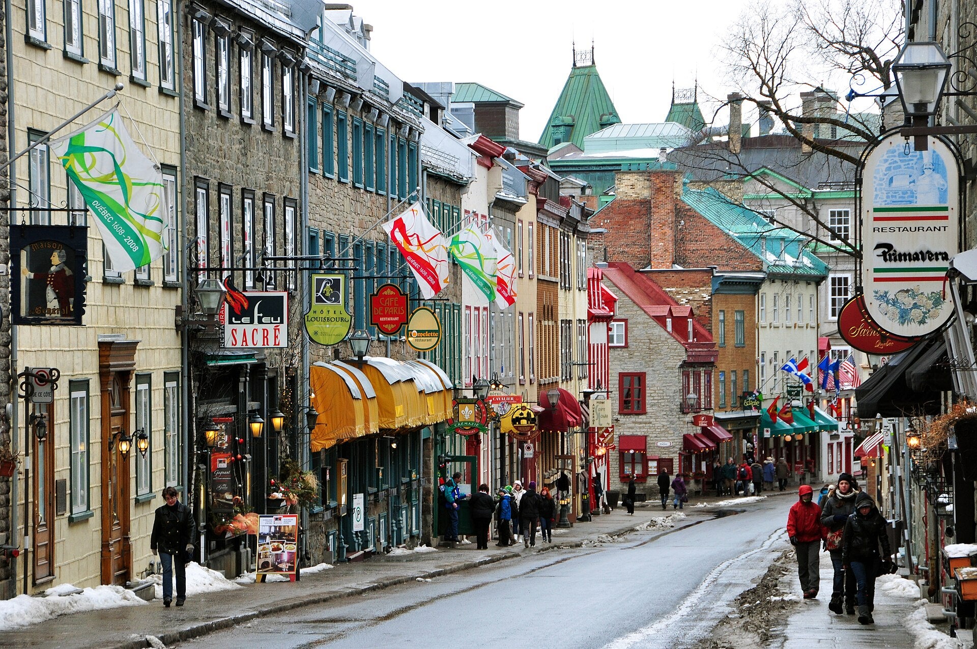 Rue Saint-Louis in Old Quebec City lined with historic stone buildings, restaurant signs and Quebec flags on a snowy winter day
