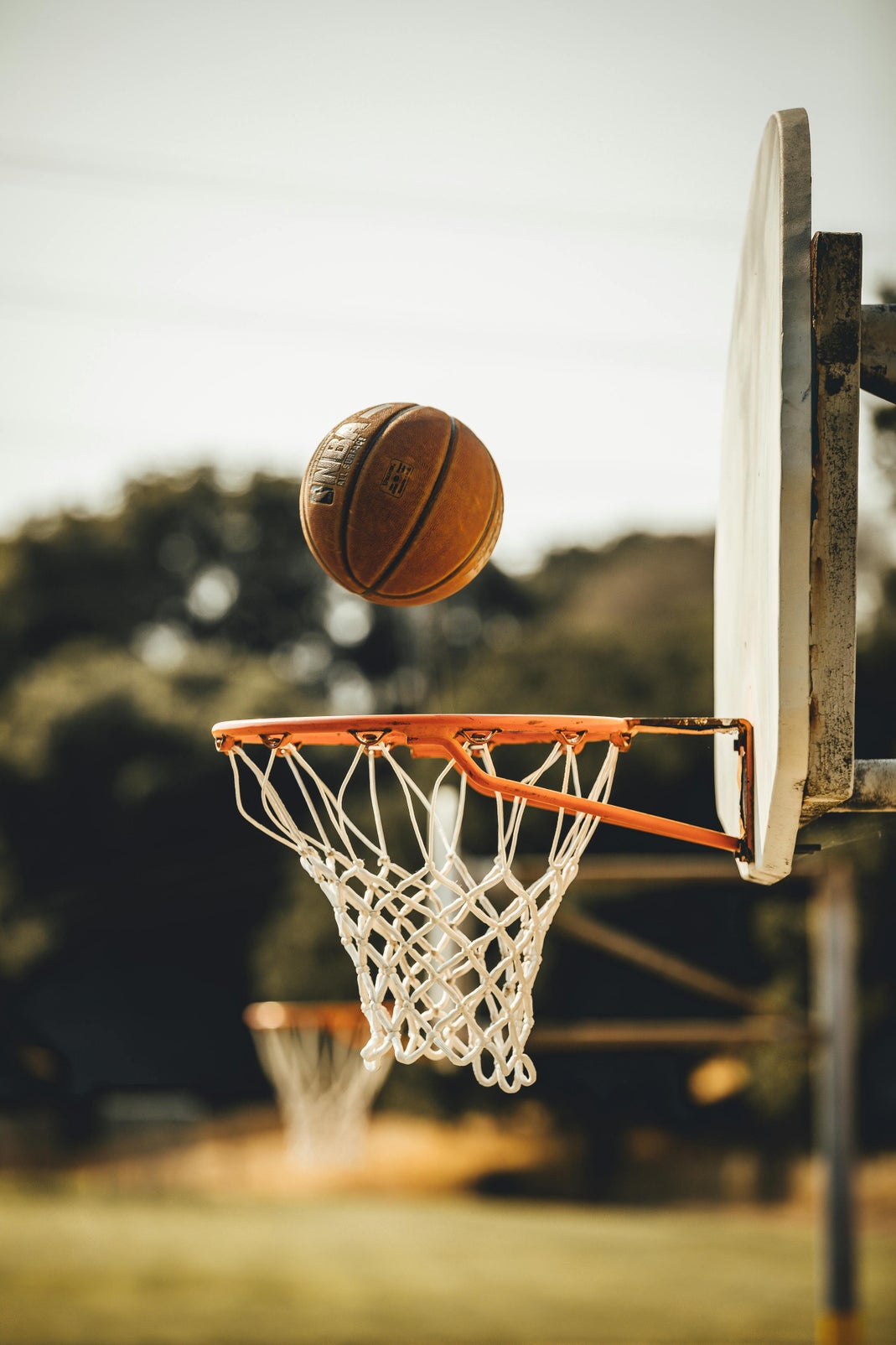 A basketball hovering above an outdoor hoop and net against a blurred tree background
