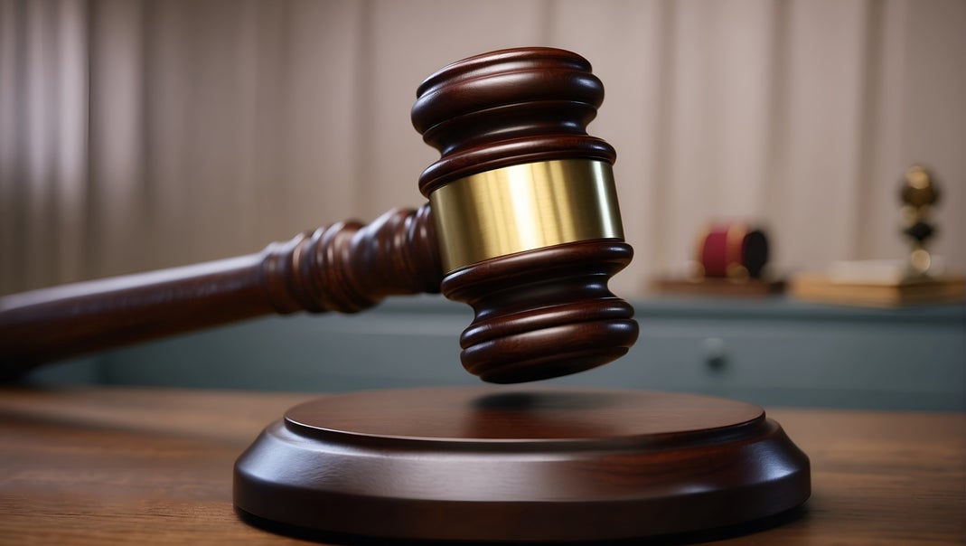 A wooden judge's gavel with a gold band striking a sound block on a courtroom desk
