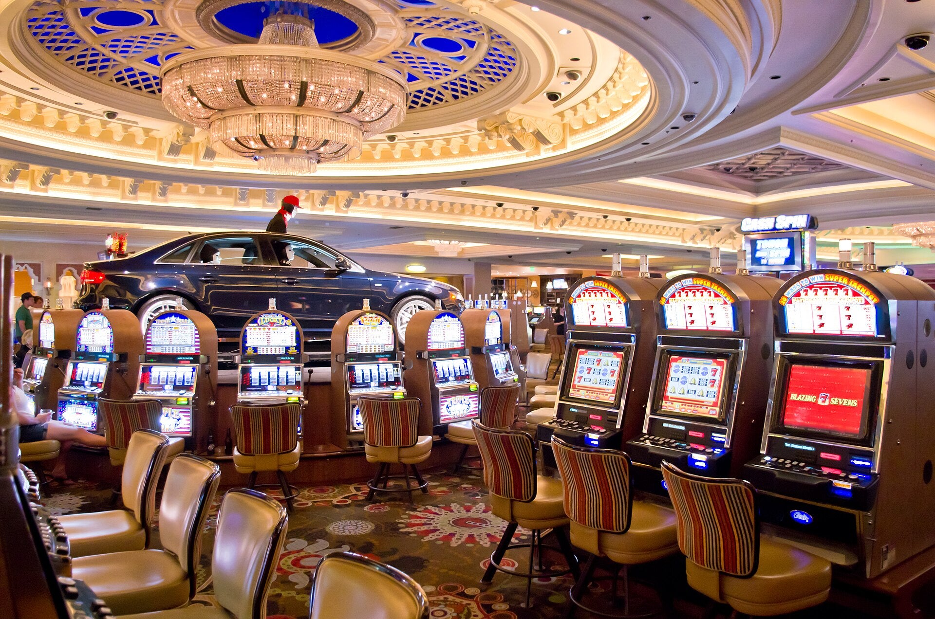 Rows of slot machines on a Las Vegas casino floor beneath a crystal chandelier