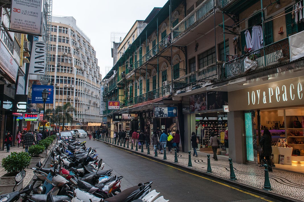 Street scene in Macau showing shops, pedestrians, and traditional balconies in the city center
