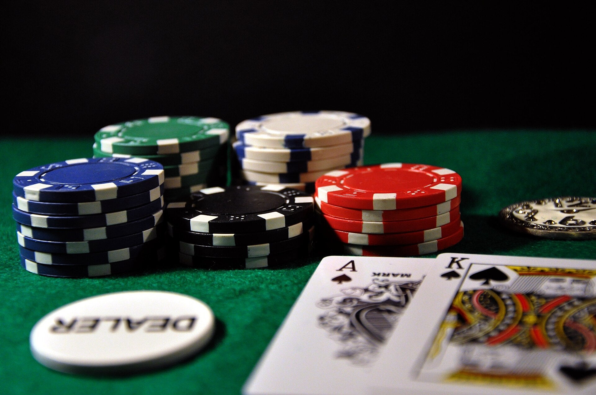 Blackjack cards showing an Ace and King of Spades next to stacked casino chips and a dealer button on a green felt table