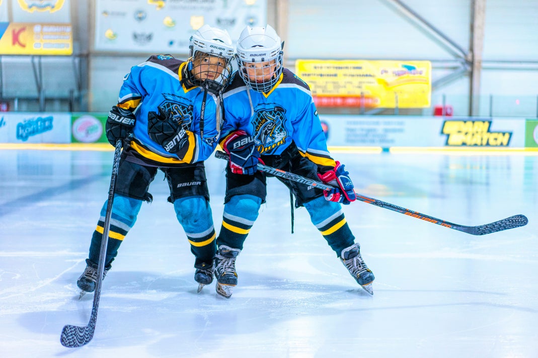 Two young hockey players in blue Bauer jerseys and helmets skating side by side on an indoor ice rink