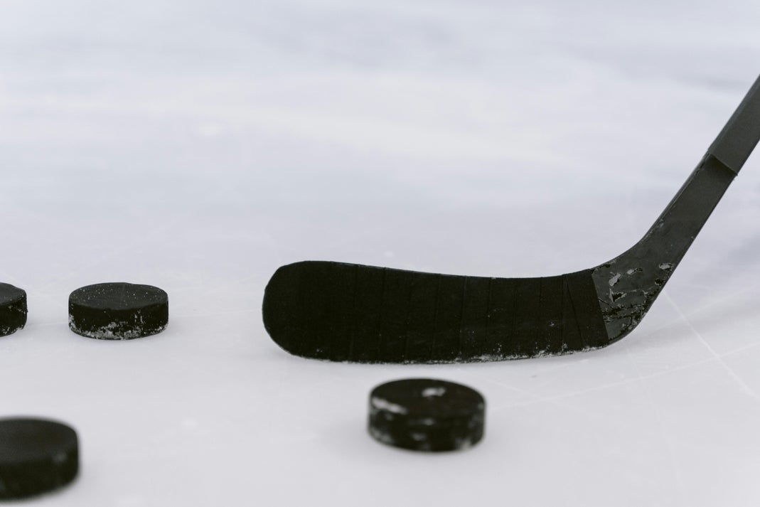 A black hockey stick blade resting on ice next to four hockey pucks