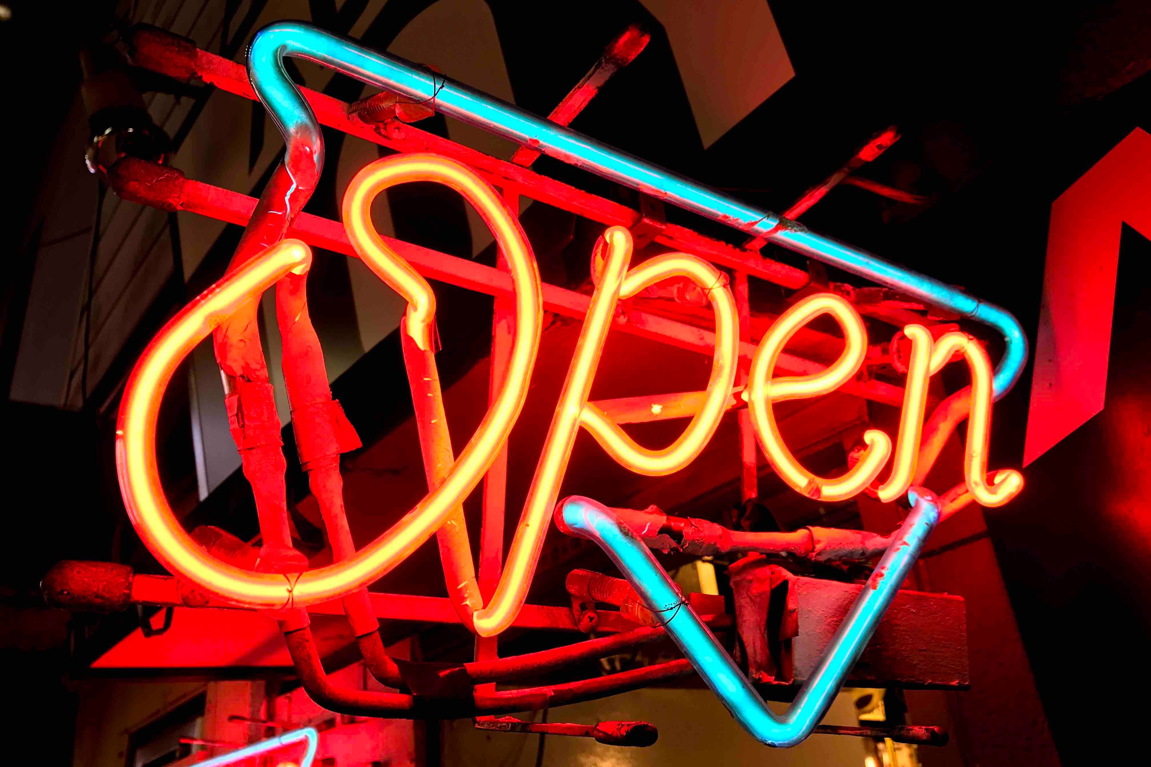 Glowing yellow and red neon Open sign with a teal border frame against a dark background