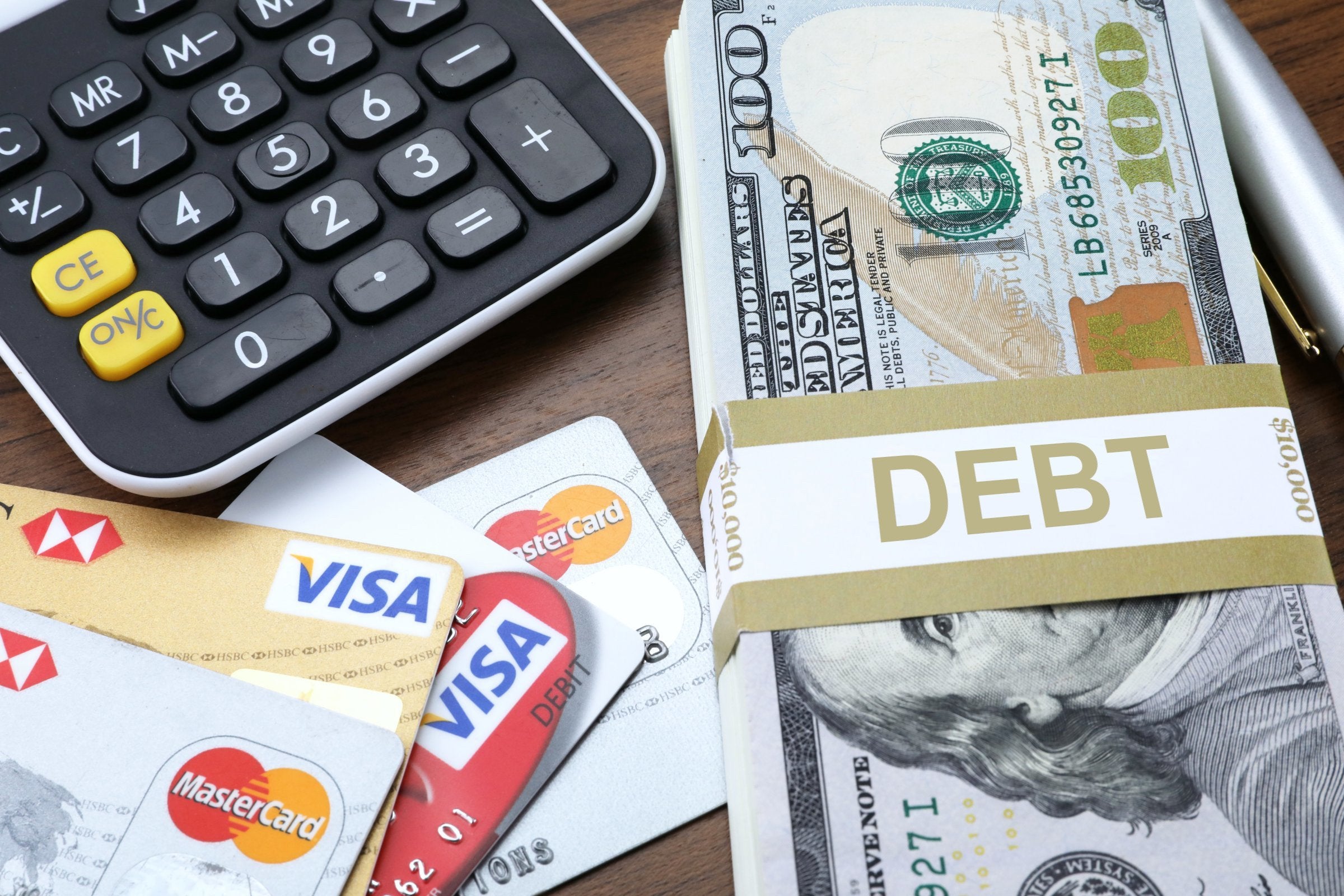 Stack of $100 bills labeled “DEBT $10,000” beside credit cards and a calculator