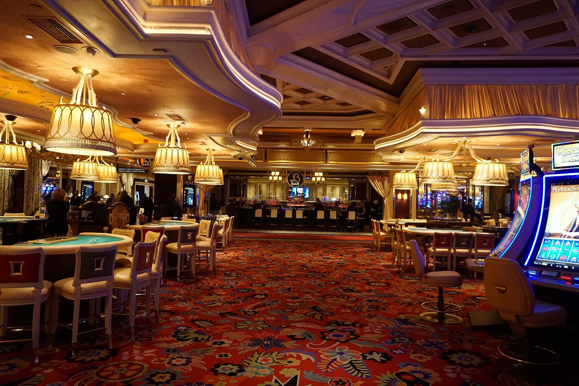 Interior of Wynn Las Vegas casino floor with chandeliers, red patterned carpet, gaming tables, and slot machines in a luxurious setting