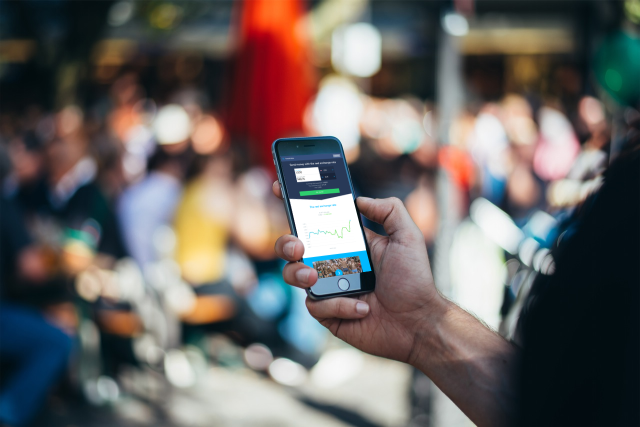 Person holding a smartphone displaying a mobile money transfer app in a crowded street
