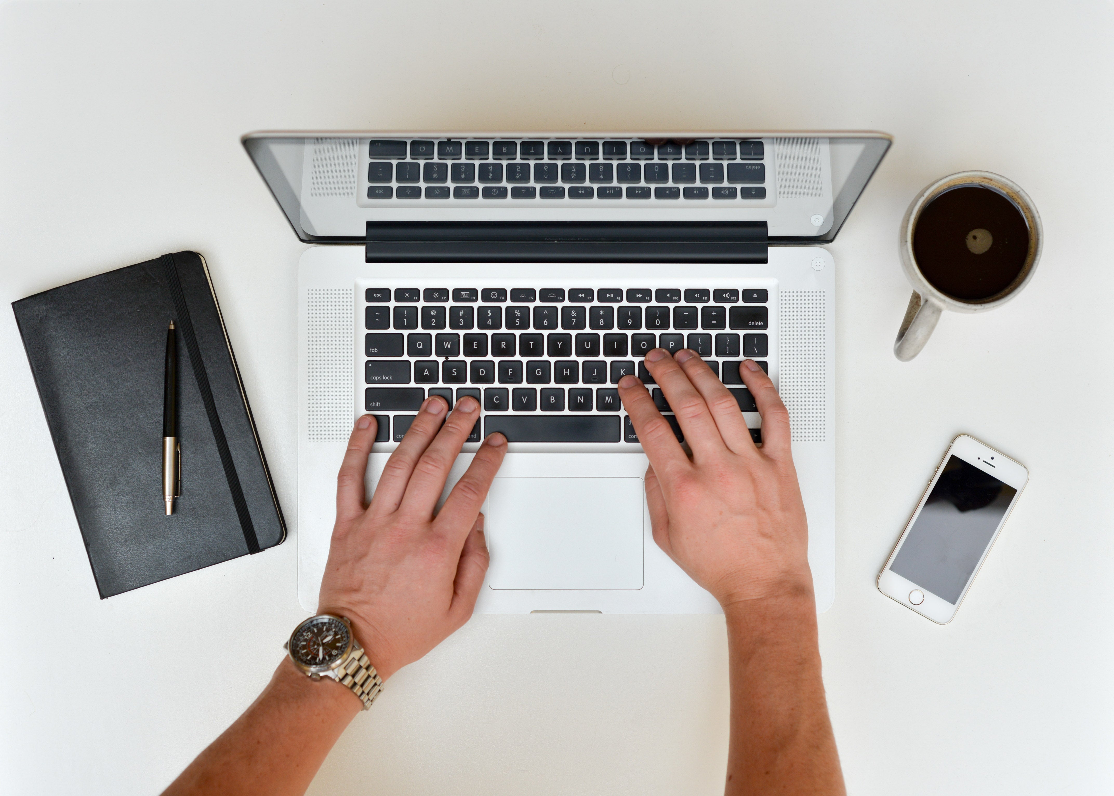 Brazil Betting Ban Could Push R$25B to Unlicensed Operators Hands typing on a laptop keyboard beside a smartphone, coffee mug and notebook, illustrating online betting in Brazil