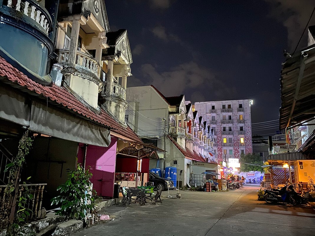 Night street view in Phuket, Thailand showing residential buildings, parked motorbikes, and lit houses