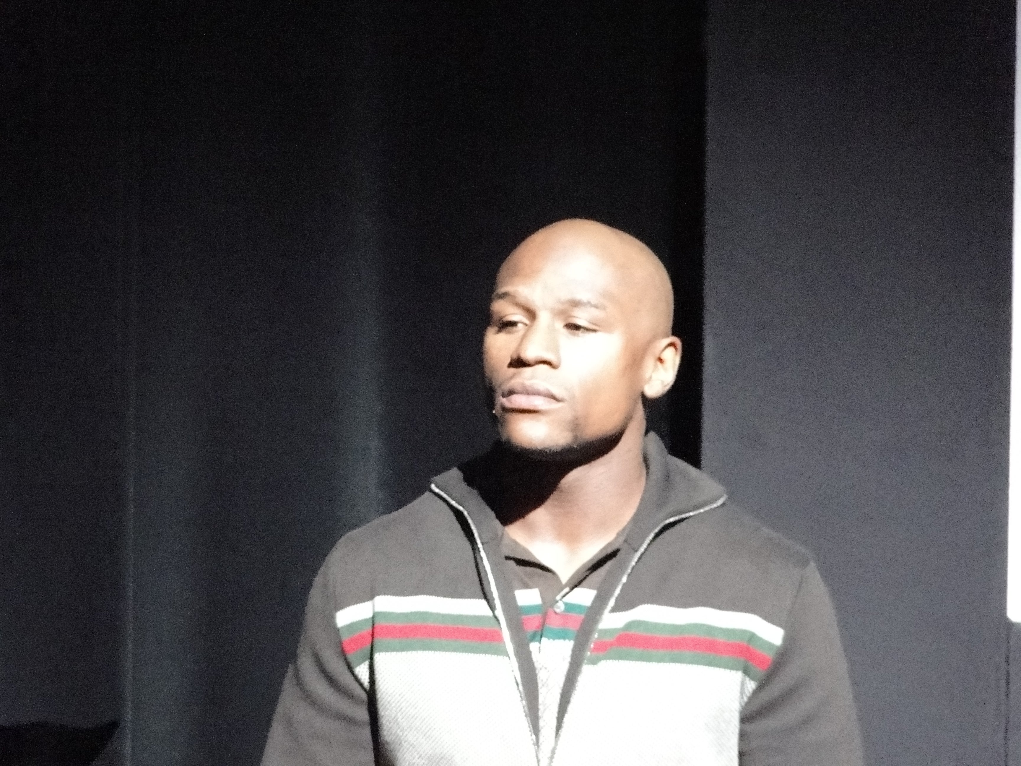 Floyd Mayweather standing on stage in a striped zip-up jacket during a public appearance