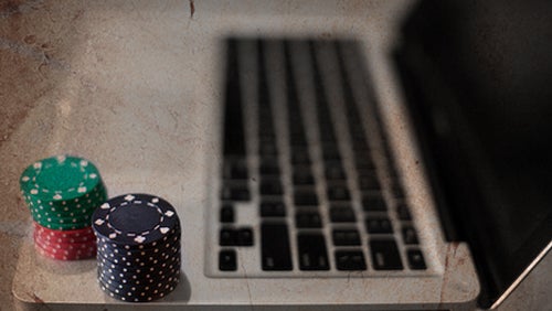 Stacks of green, red, and black poker chips next to a laptop keyboard, representing online gambling