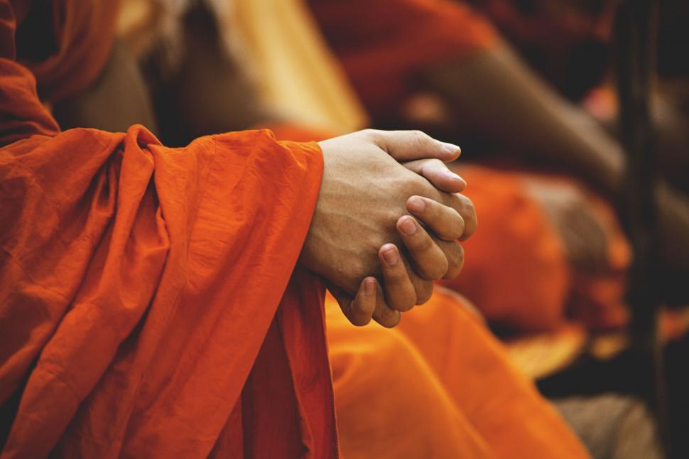 Buddhist monk in orange robes sitting with clasped hands