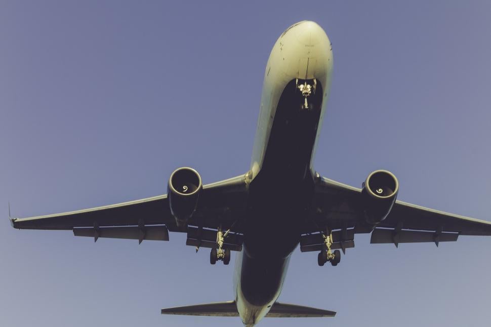 Close-up view of a commercial passenger airplane from below with landing gear deployed against a clear blue sky