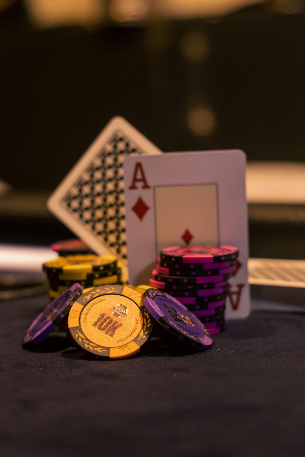 Yellow, purple, and pink casino chips stacked next to an ace of diamonds playing card on a dark casino table