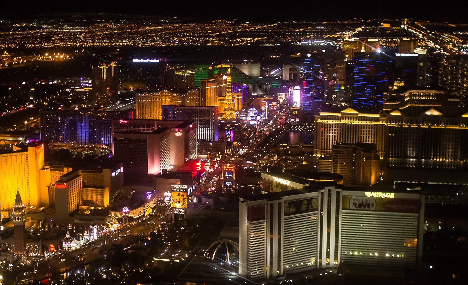 Aerial night view of the Las Vegas Strip showing illuminated casino resorts including Caesars Palace, The Mirage, and Harrah's