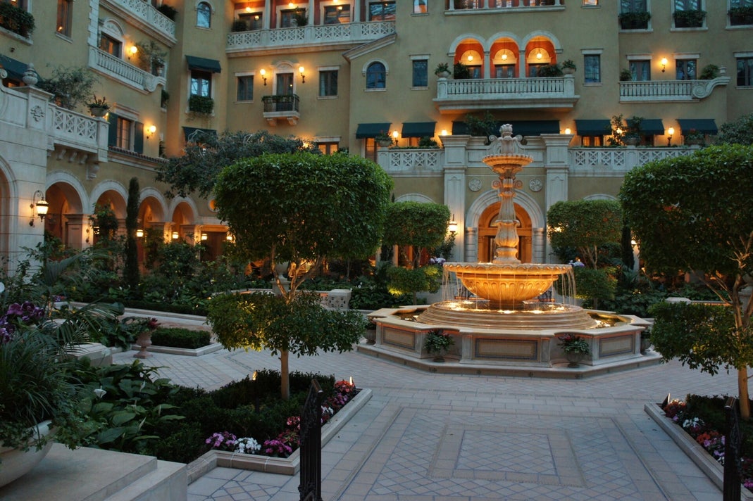 The courtyard of the MGM Grand Mansion in Las Vegas, featuring a lit fountain, manicured trees, and the facade of the upscale private retreat