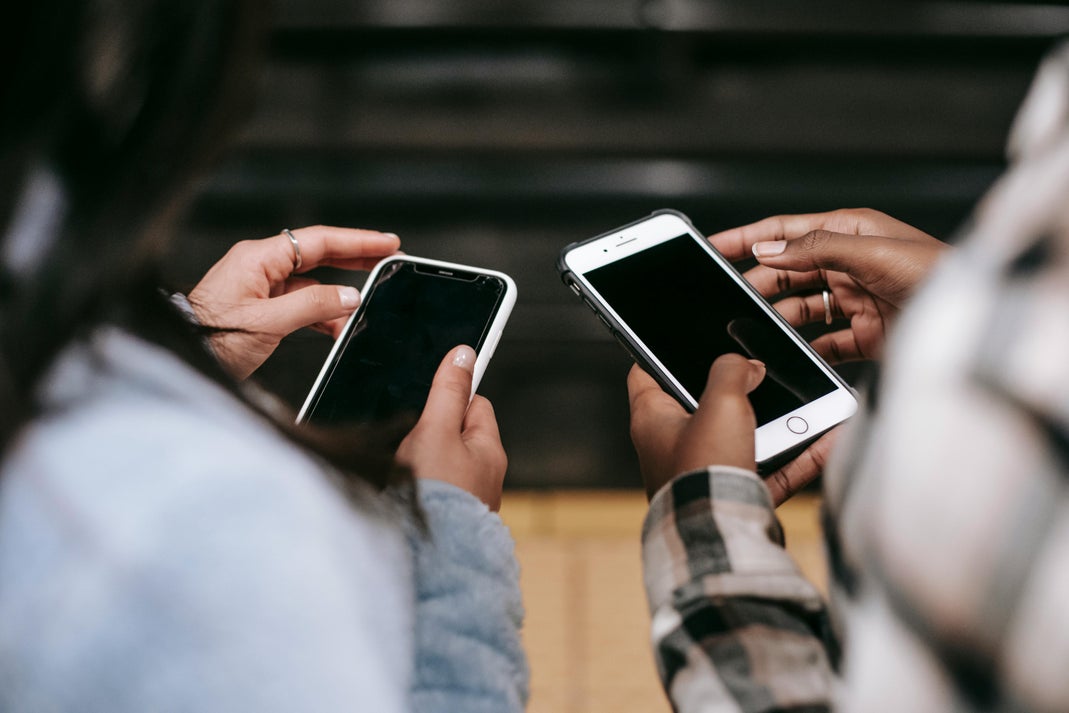 Two people sitting side by side, each holding a smartphone with a black screen