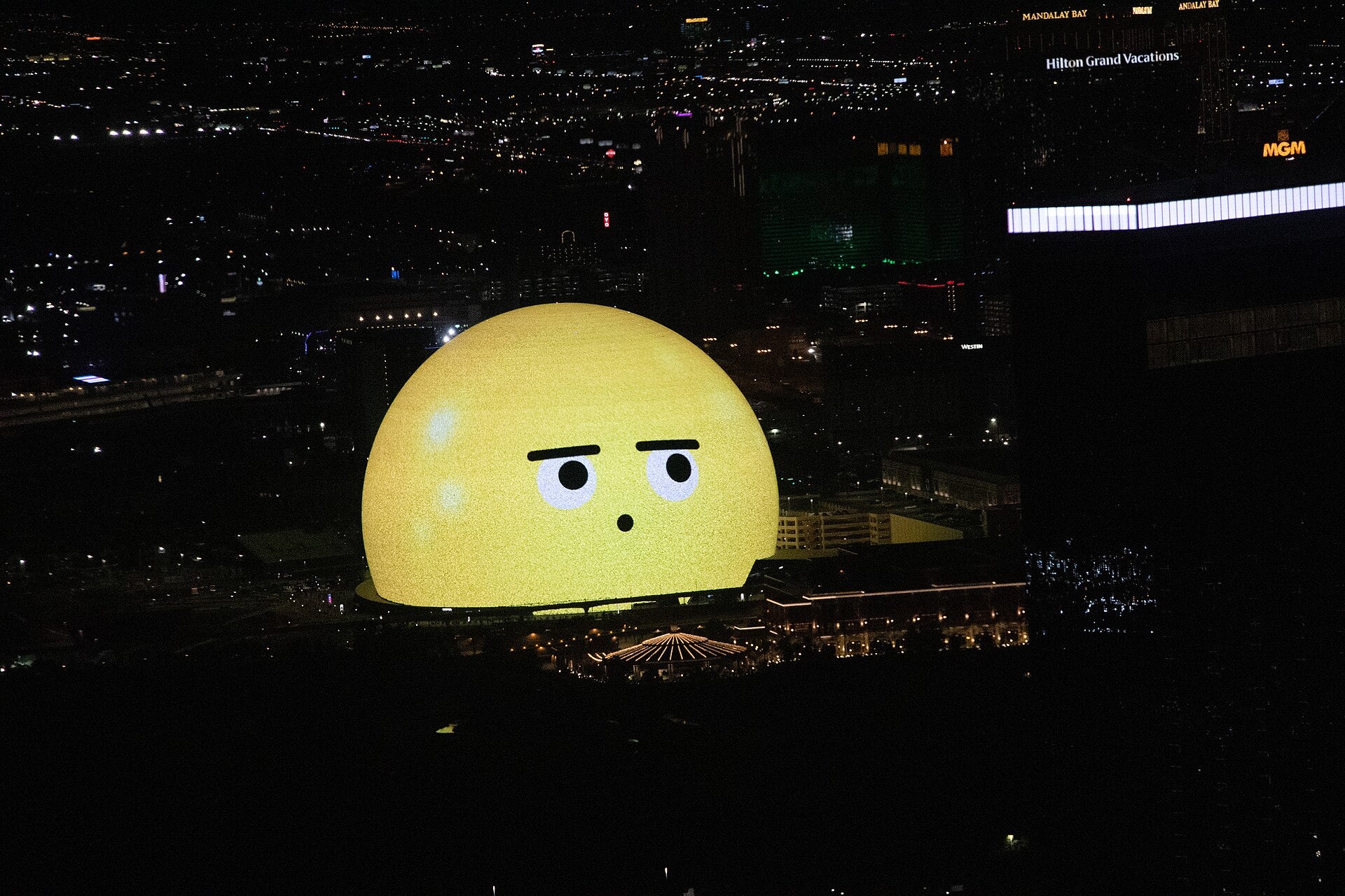 Sphere Las Vegas lit up at night with a large emoji face on its exterior, surrounded by the city skyline