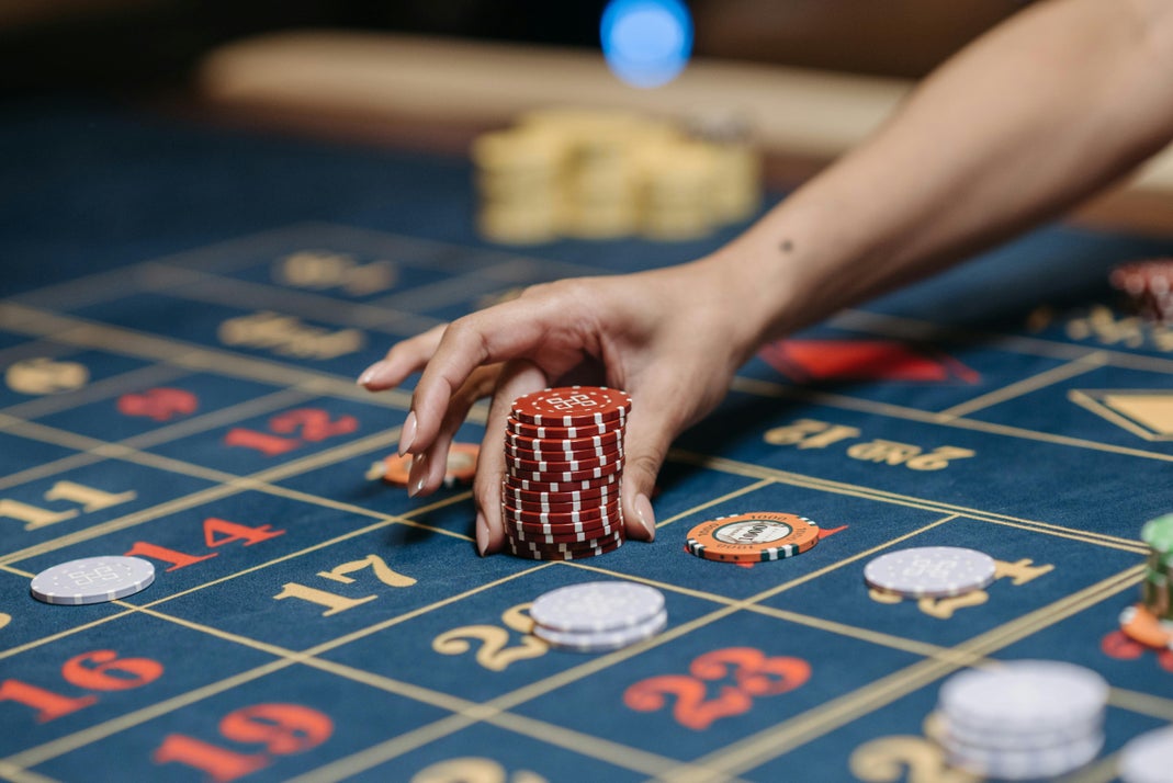A hand placing a stack of red casino chips on a roulette betting table
