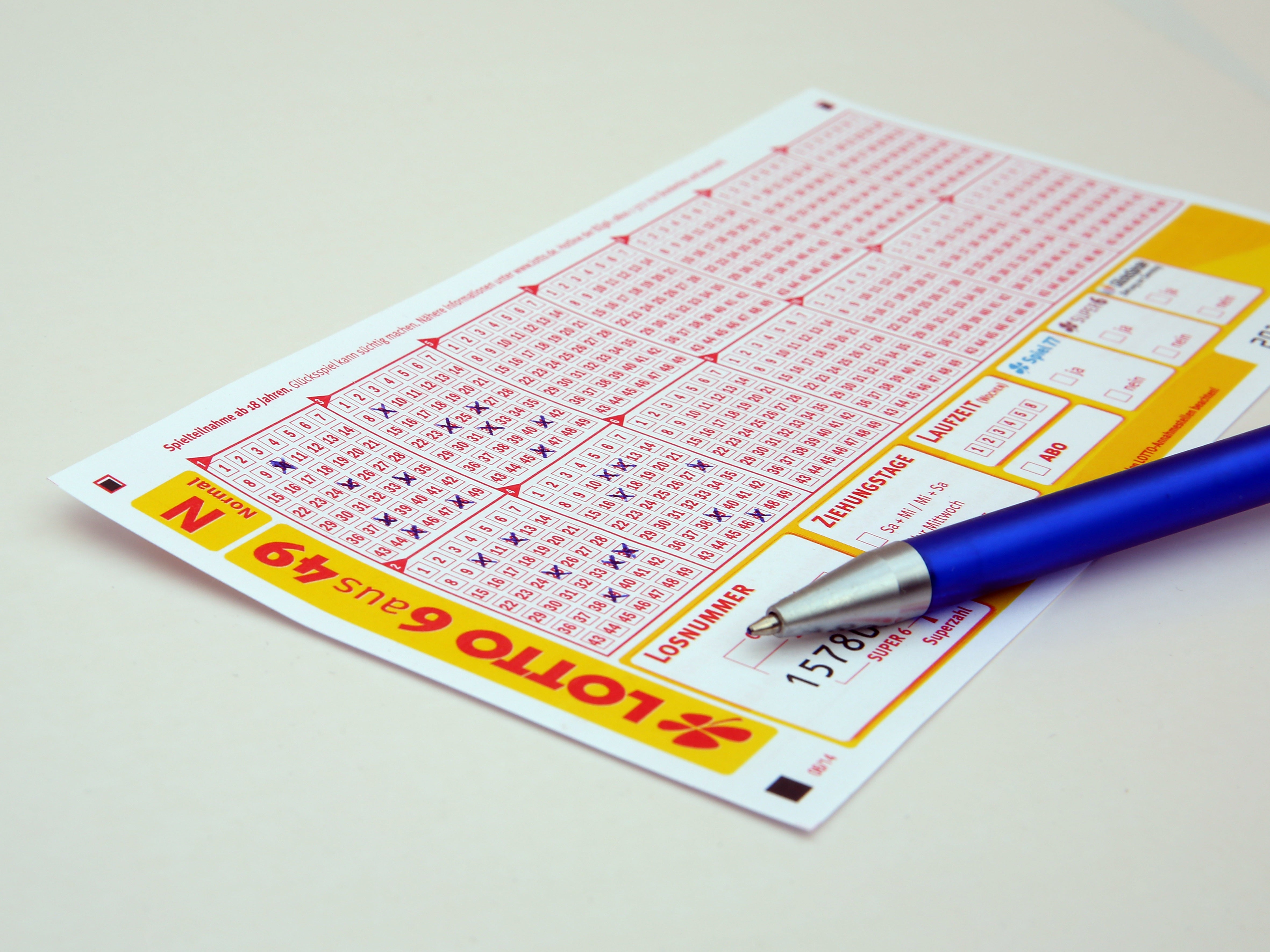 A Lotto 6 aus 49 lottery ticket with hand-marked numbers and a blue ballpoint pen on a white surface