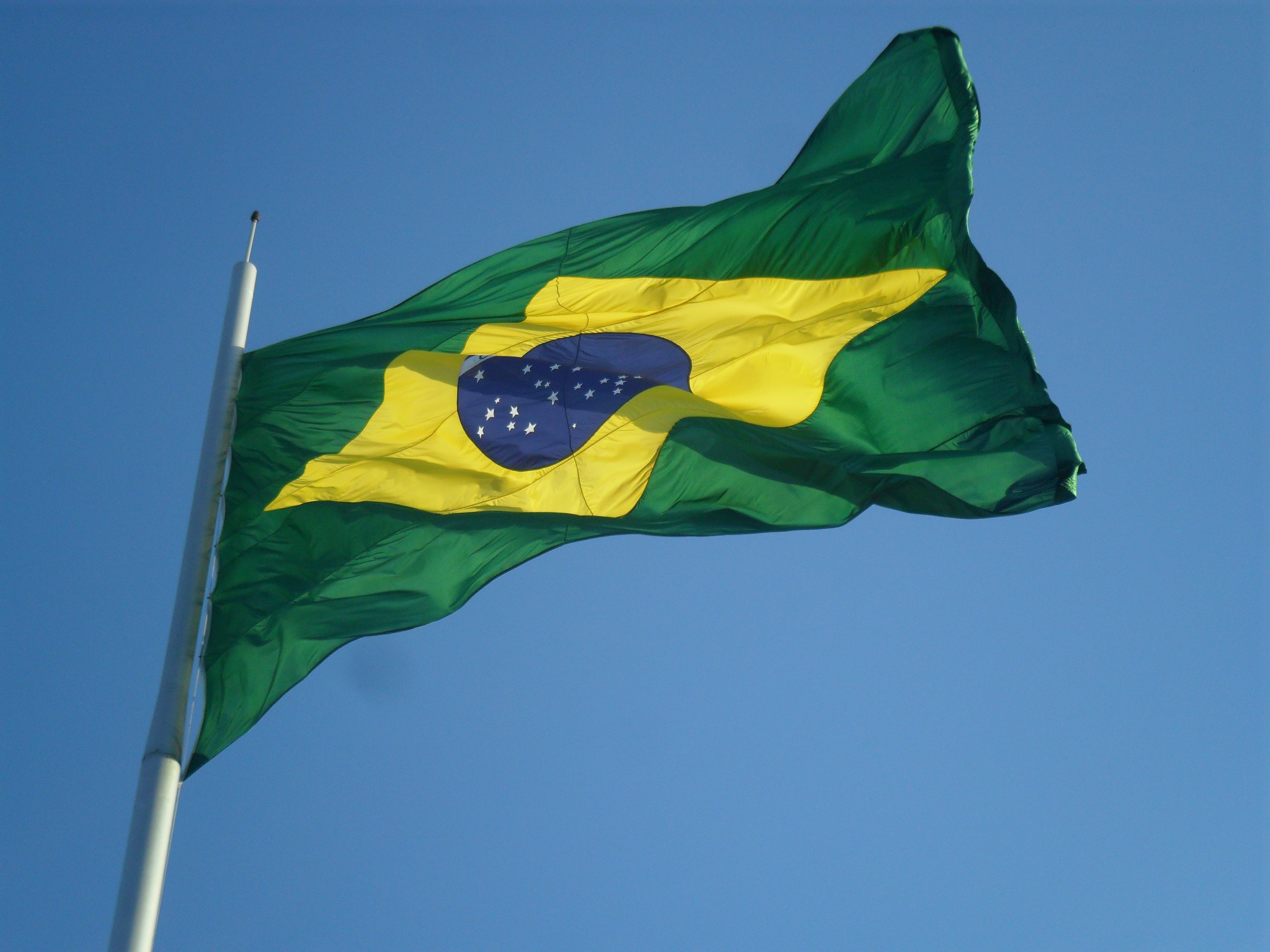 Brazilian flag waving on a white flagpole against a clear blue sky