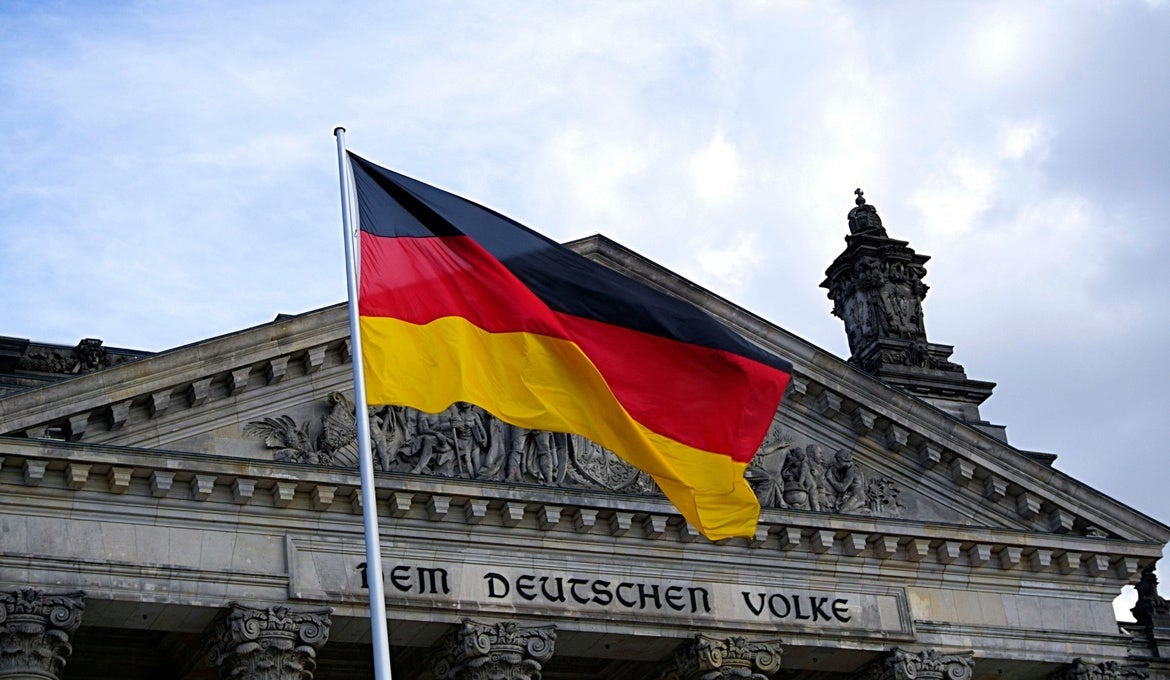 An image of a German flag flying in front of an old stone building