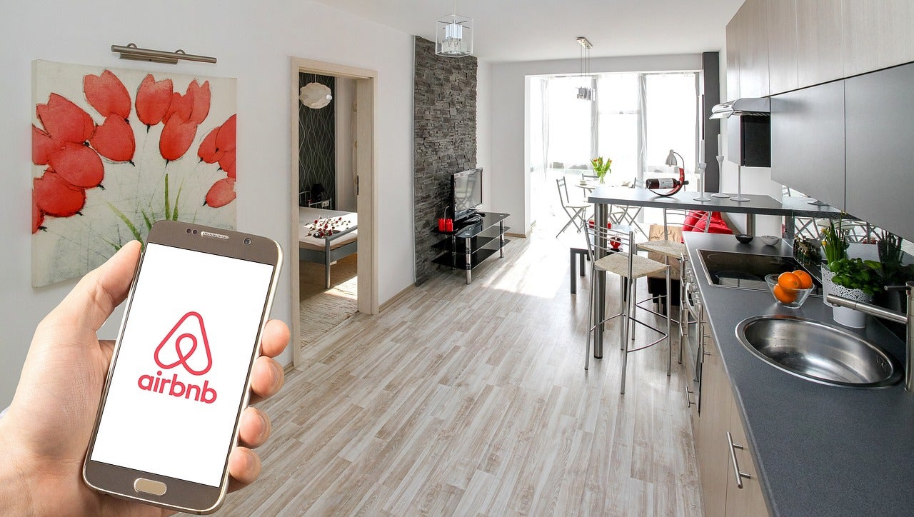 Hand holding smartphone with Airbnb app open inside a modern rental apartment