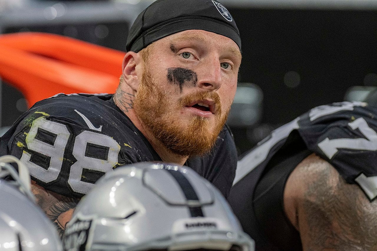Close-up of Maxx Crosby wearing a Las Vegas Raiders jersey number 98 with eye black, sitting on the sideline during a game
