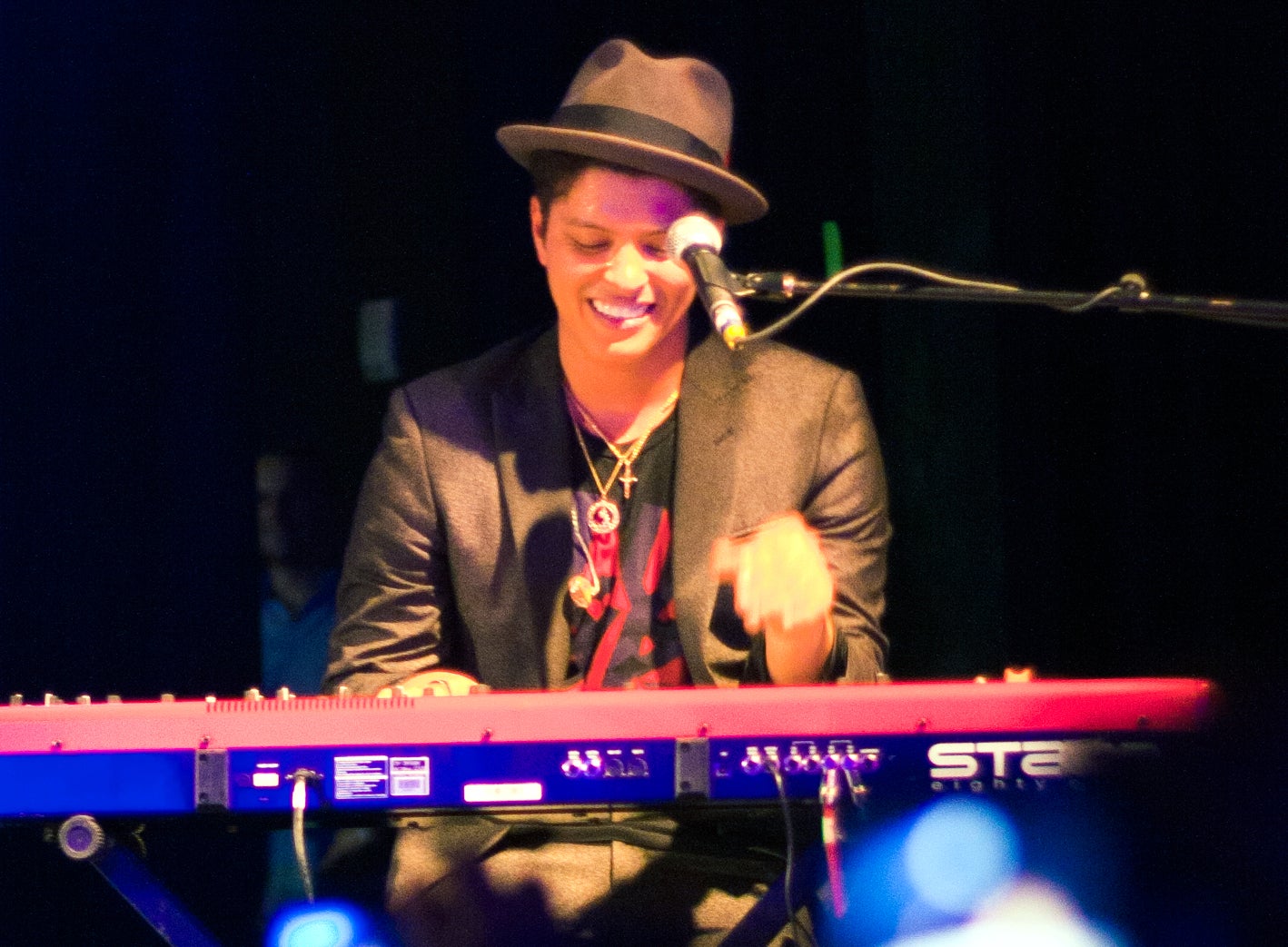 Bruno Mars smiling while playing a red keyboard on stage