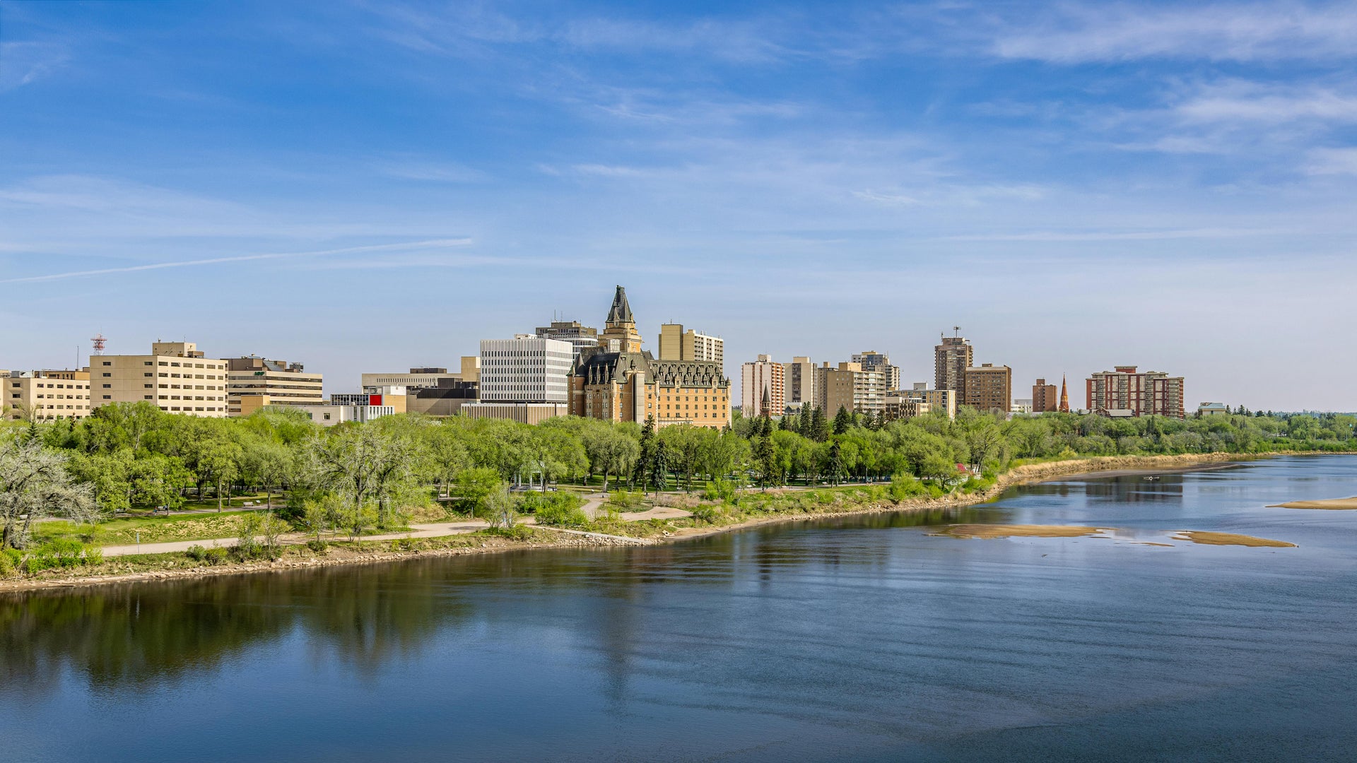 Downtown Saskatoon skyline with Delta Bessborough hotel and riverbank park along the South Saskatchewan River in spring