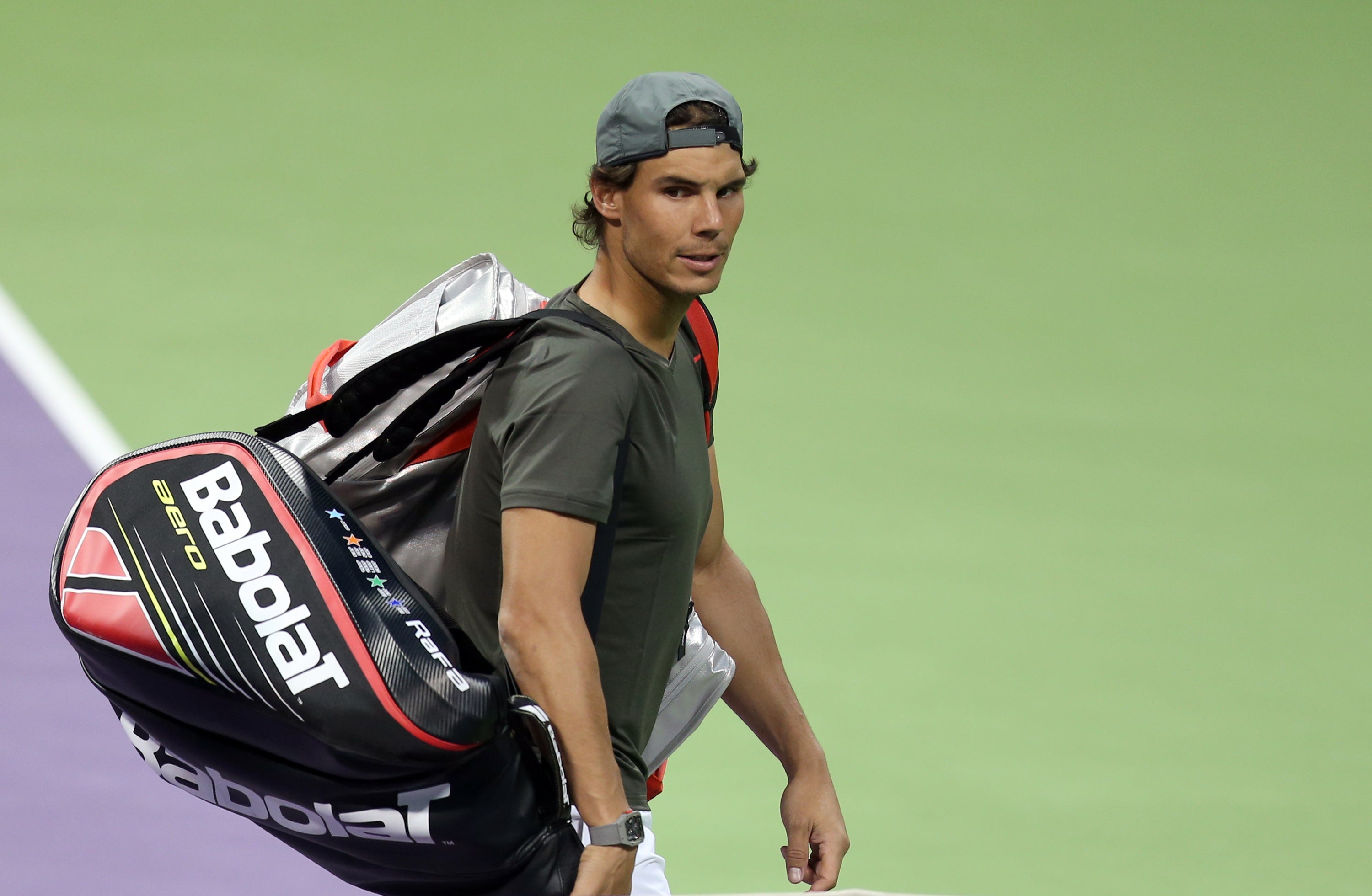 Rafael Nadal carries his tennis bag off a hard court after a training session in Doha, Qatar