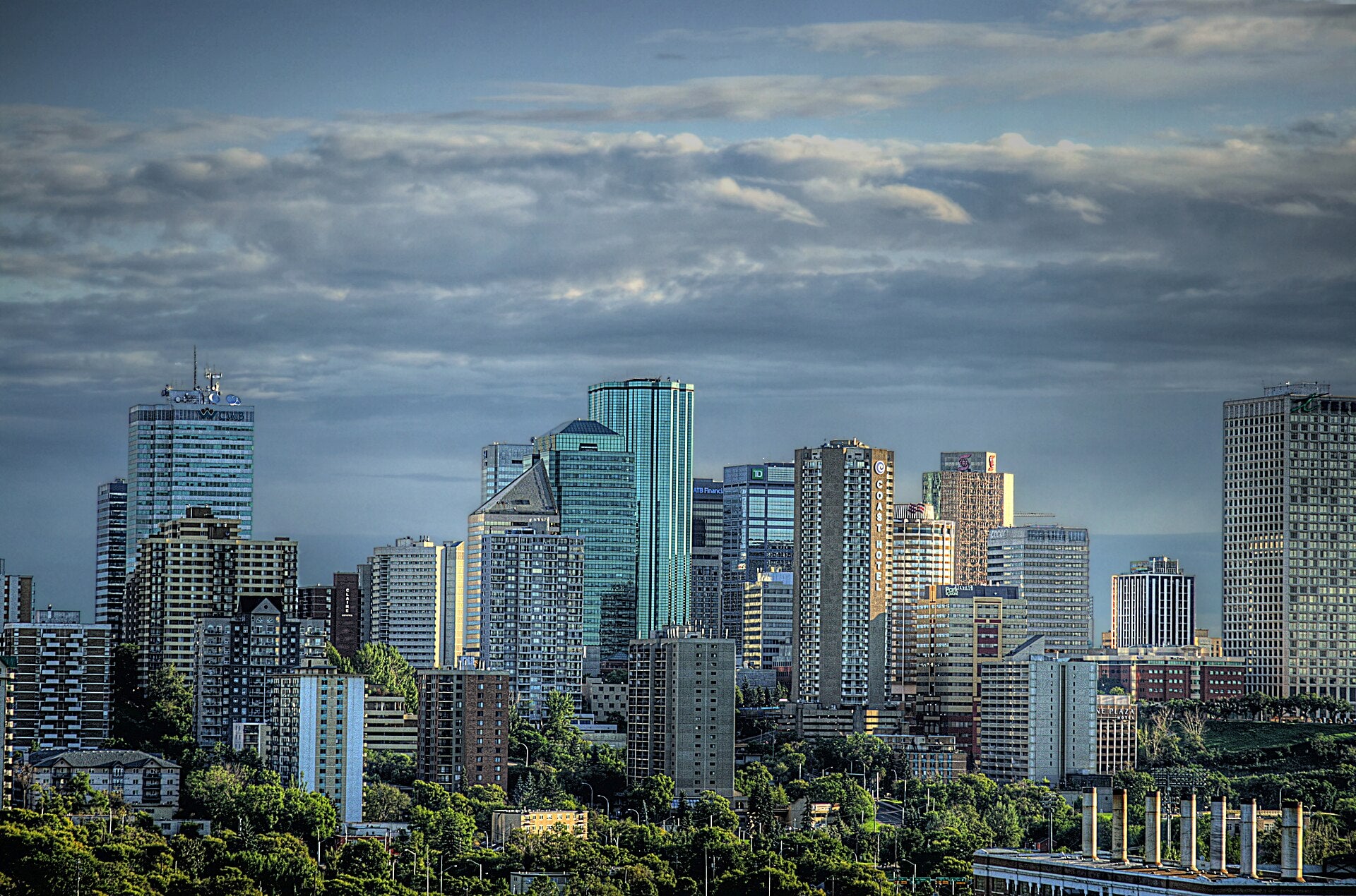 Edmonton, Alberta skyline with downtown towers and tree-lined foreground under a cloudy sky