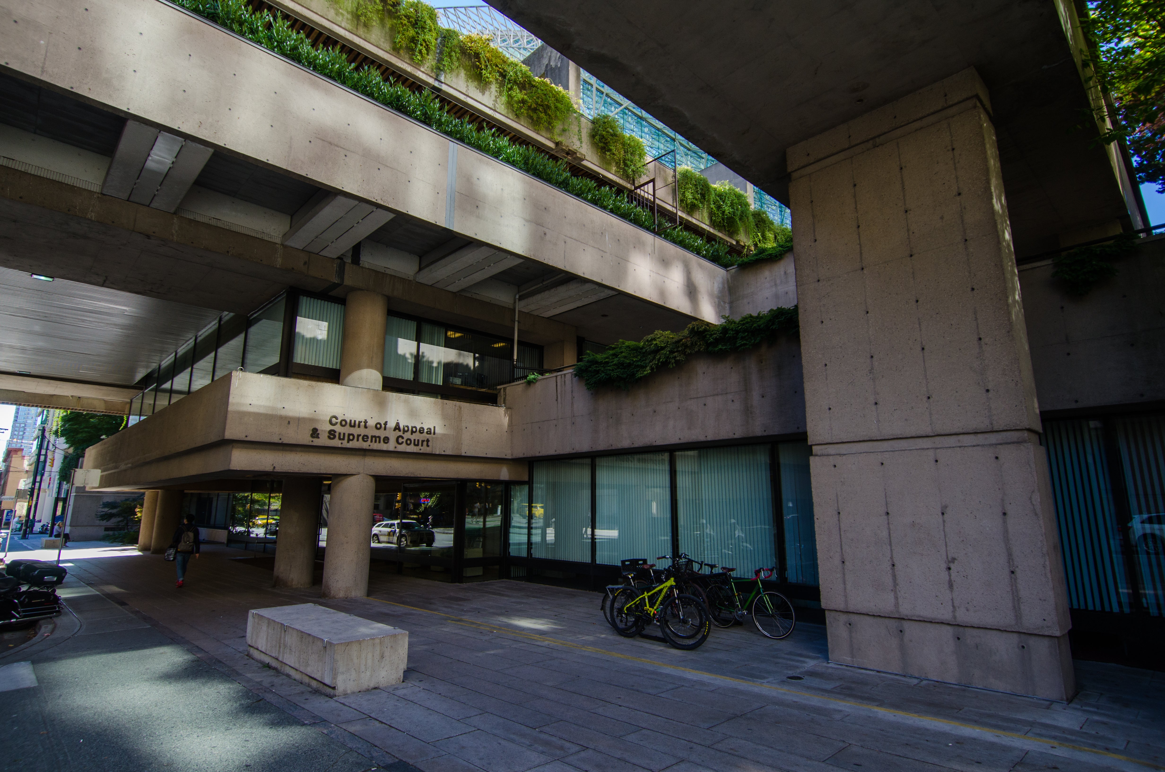 Concrete exterior of the British Columbia Court of Appeal and Supreme Court building in Vancouver, featuring brutalist architecture with layered walkways, greenery, and bicycles at street level