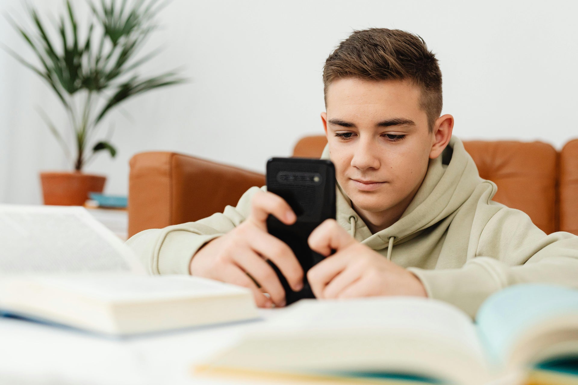 Young male looking at smartphone surrounded by open books