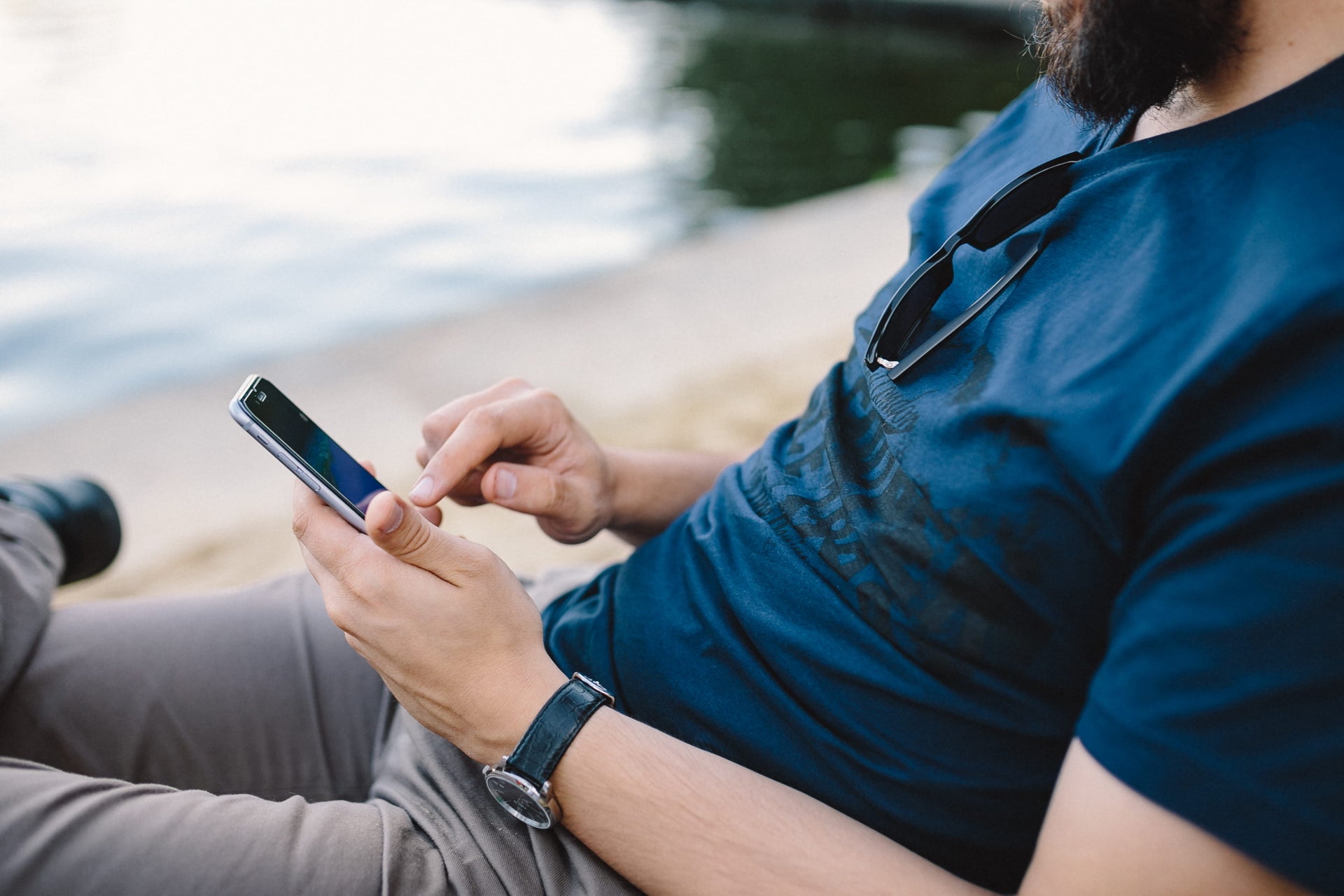 Man in blue t-shirt using a smartphone while sitting on a beach