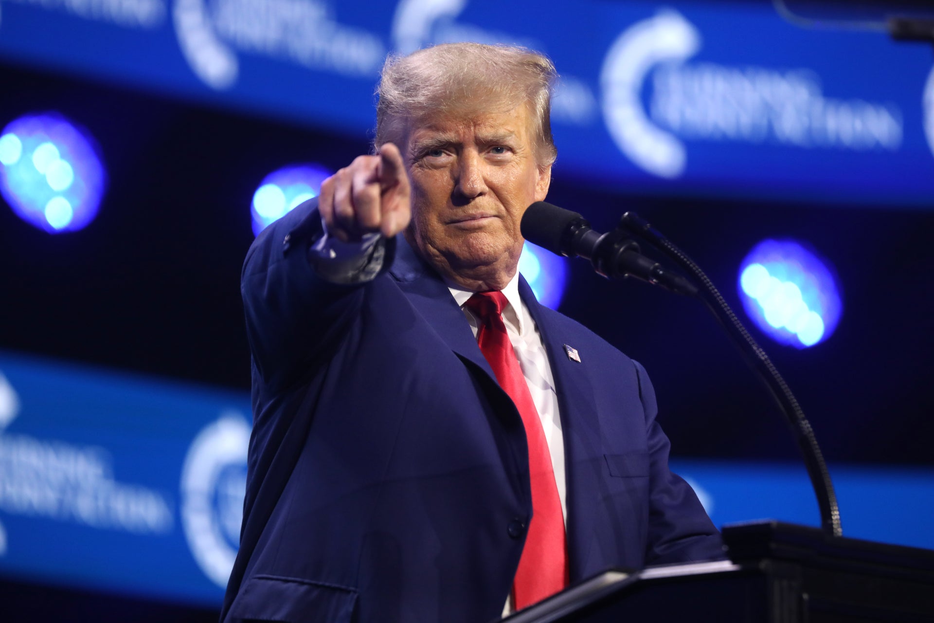 President Donald Trump pointing at the crowd while speaking at a podium during a 2023 event