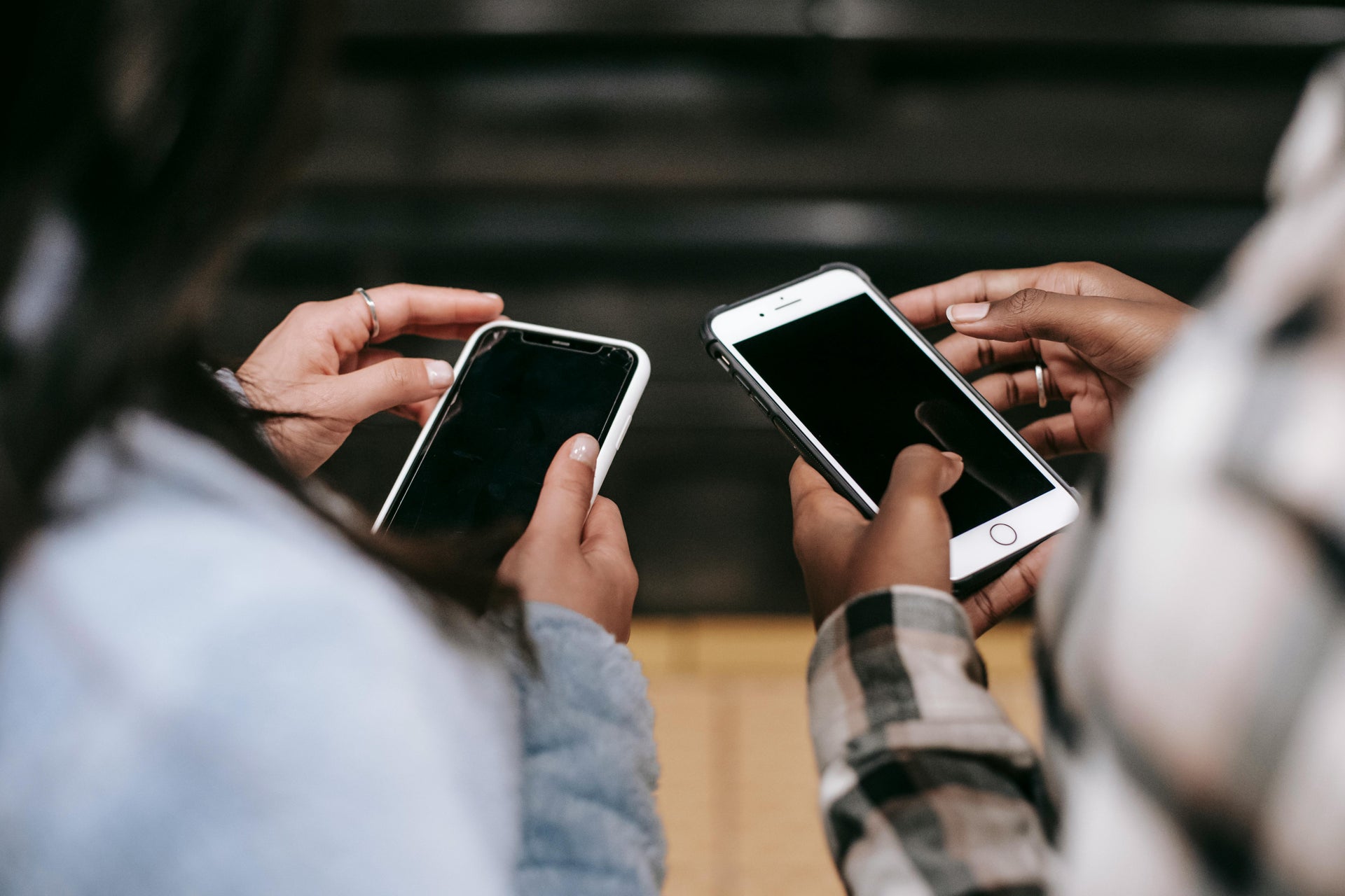 Two people sitting side by side, each holding a smartphone with a black screen