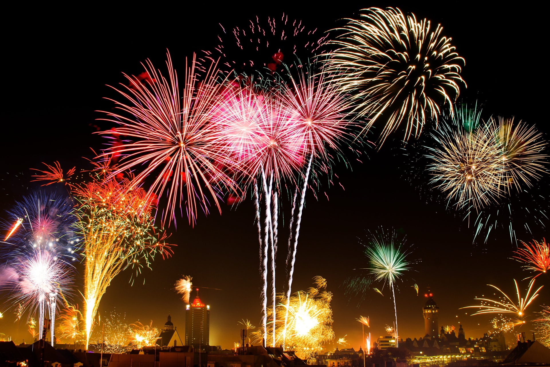 Colorful fireworks bursting over a city skyline at night during a large outdoor celebration