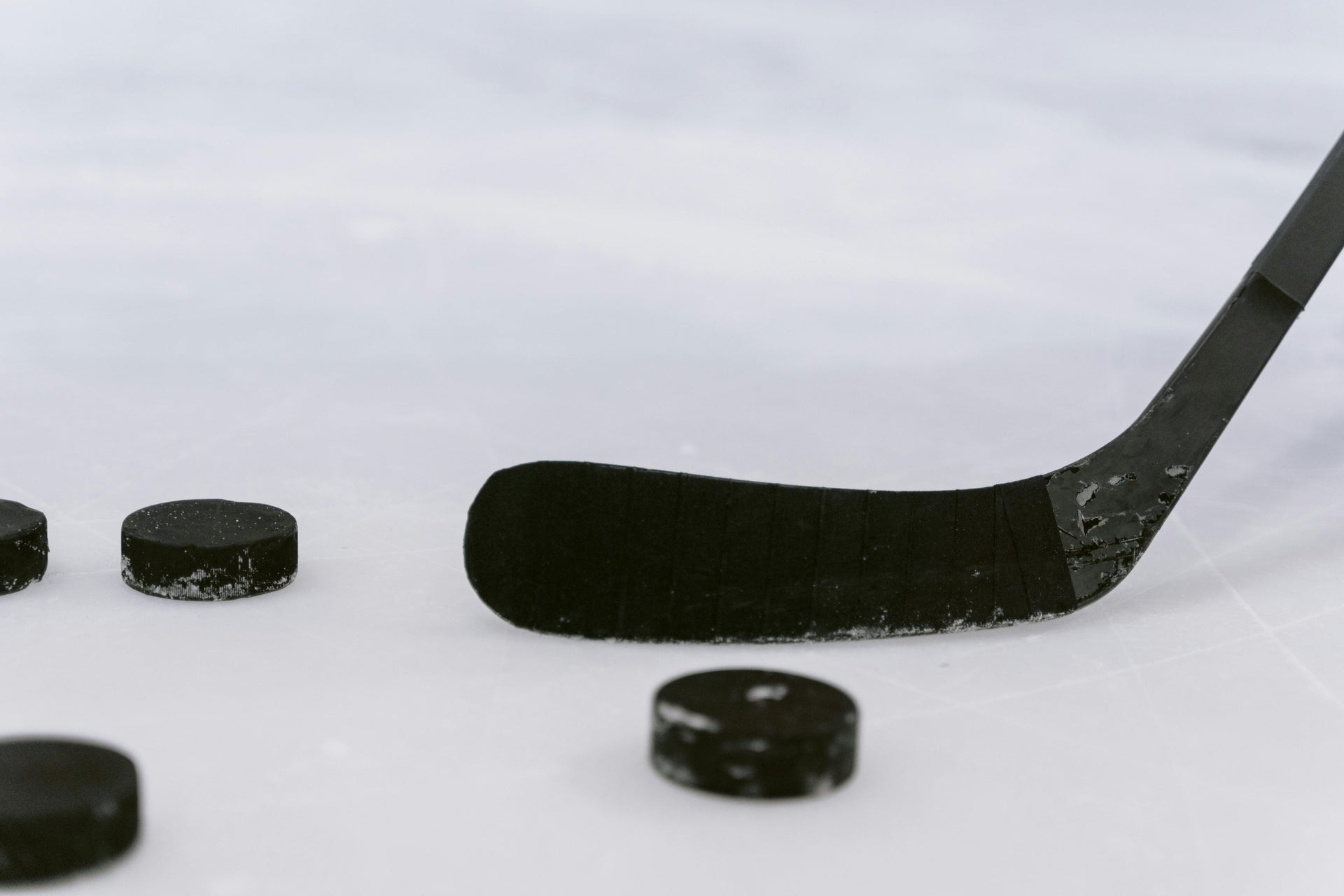 A black hockey stick blade resting on ice next to four hockey pucks
