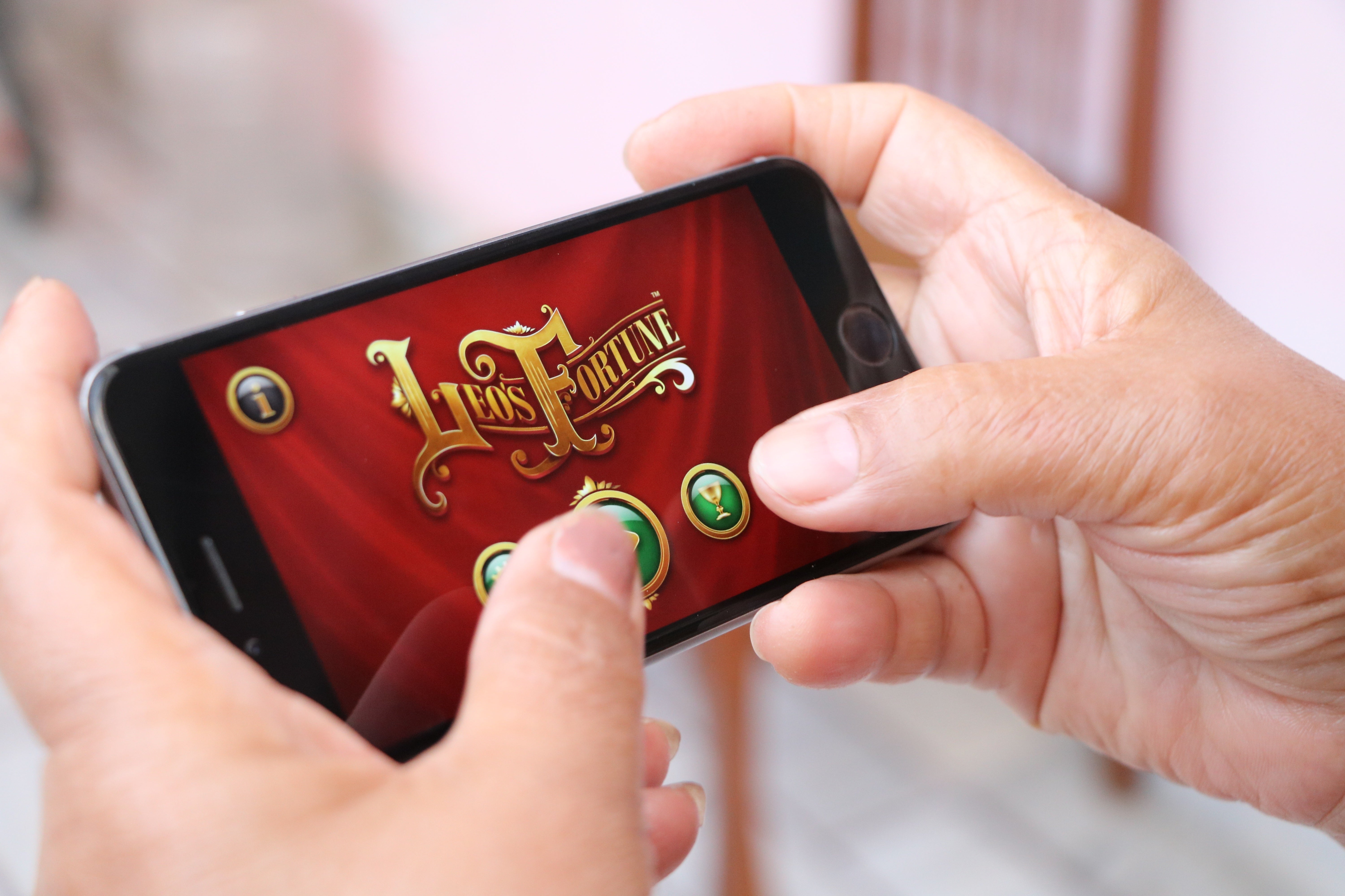 A person holds a smartphone sideways with both hands and taps the start screen of a mobile game