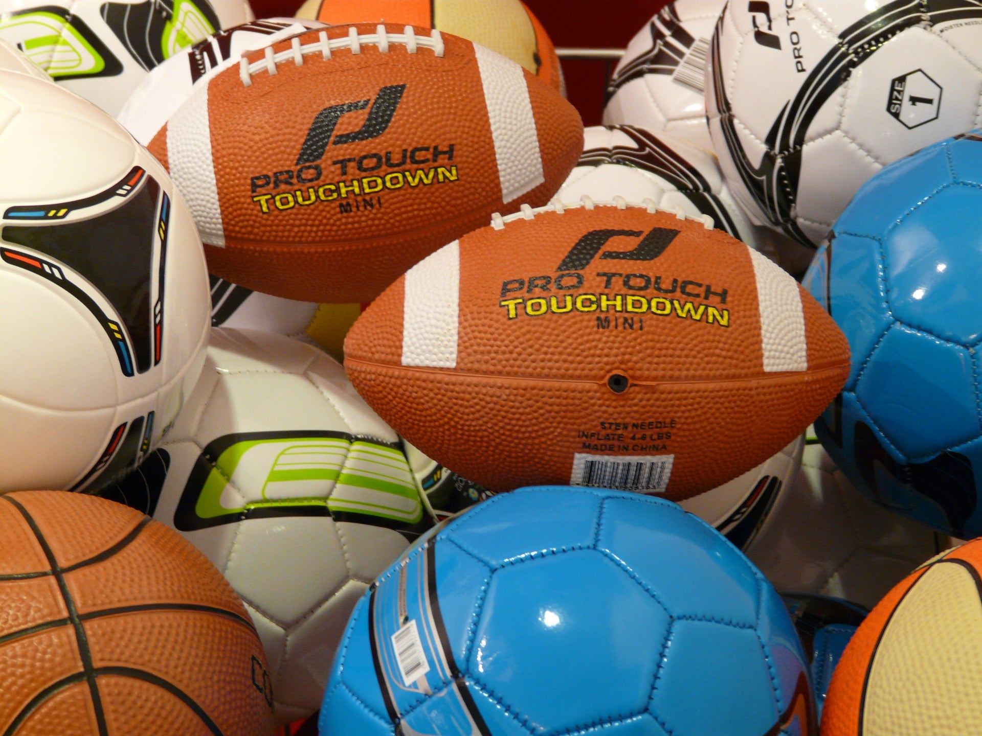 American footballs, soccer balls and a basketball grouped together as sports equipment