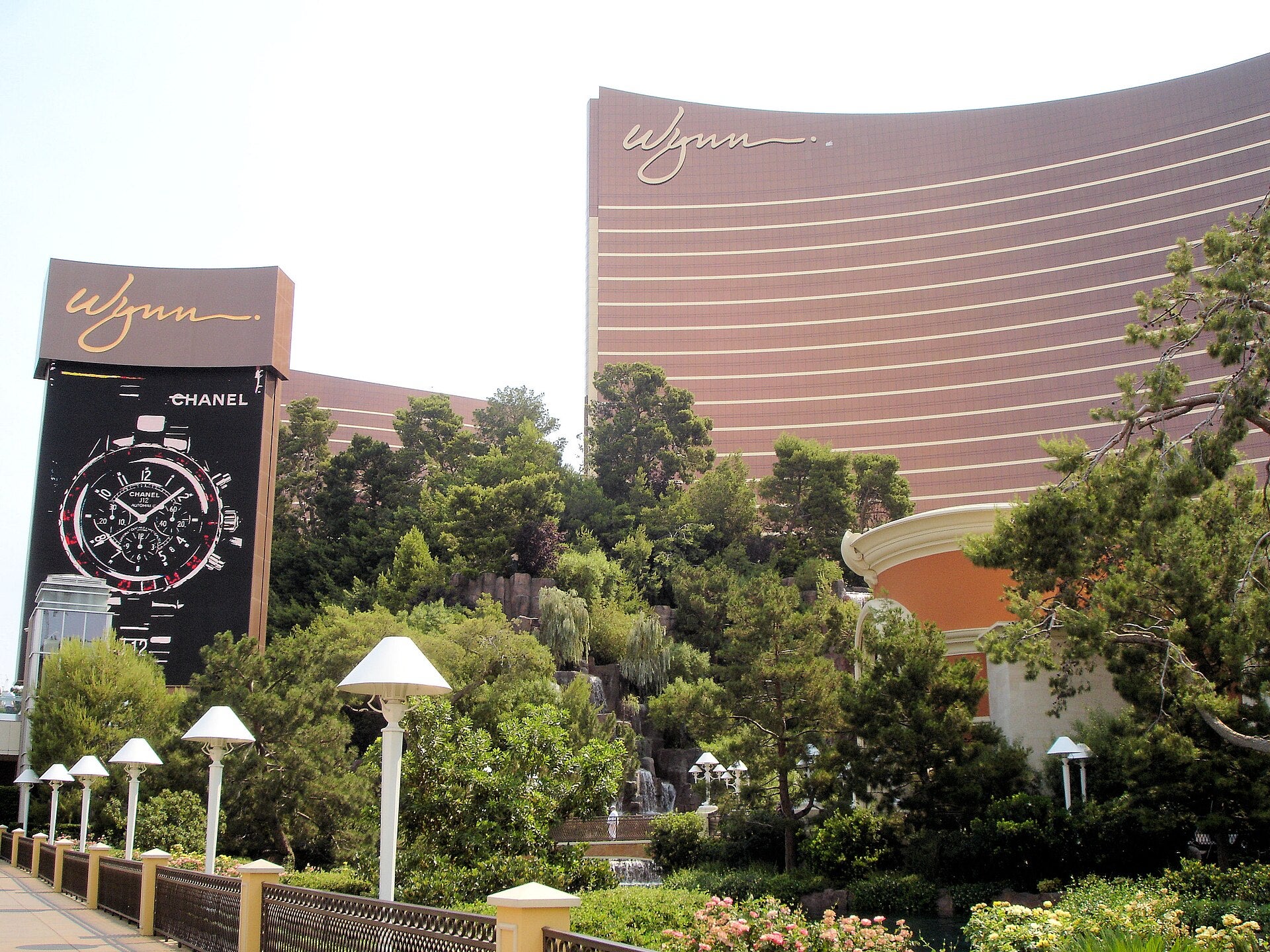G2E 2026: Global Gaming Expo Heads to Las Vegas Sept. 28 Wynn Las Vegas resort and casino with curved golden logo building, landscaped walkway, waterfall, and luxury signage highlighting the iconic Strip property