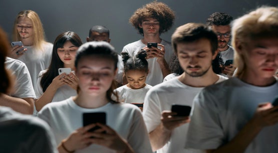 Group of people in white shirts staring at smartphones in a dimly lit studio, highlighting technology dependence and social disconnection