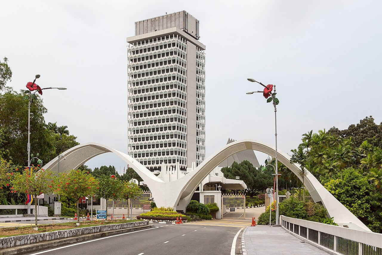 Entrance gate and tower of Malaysian Parliament in Kuala Lumpur, framed by hibiscus street lamps and landscaped gardens