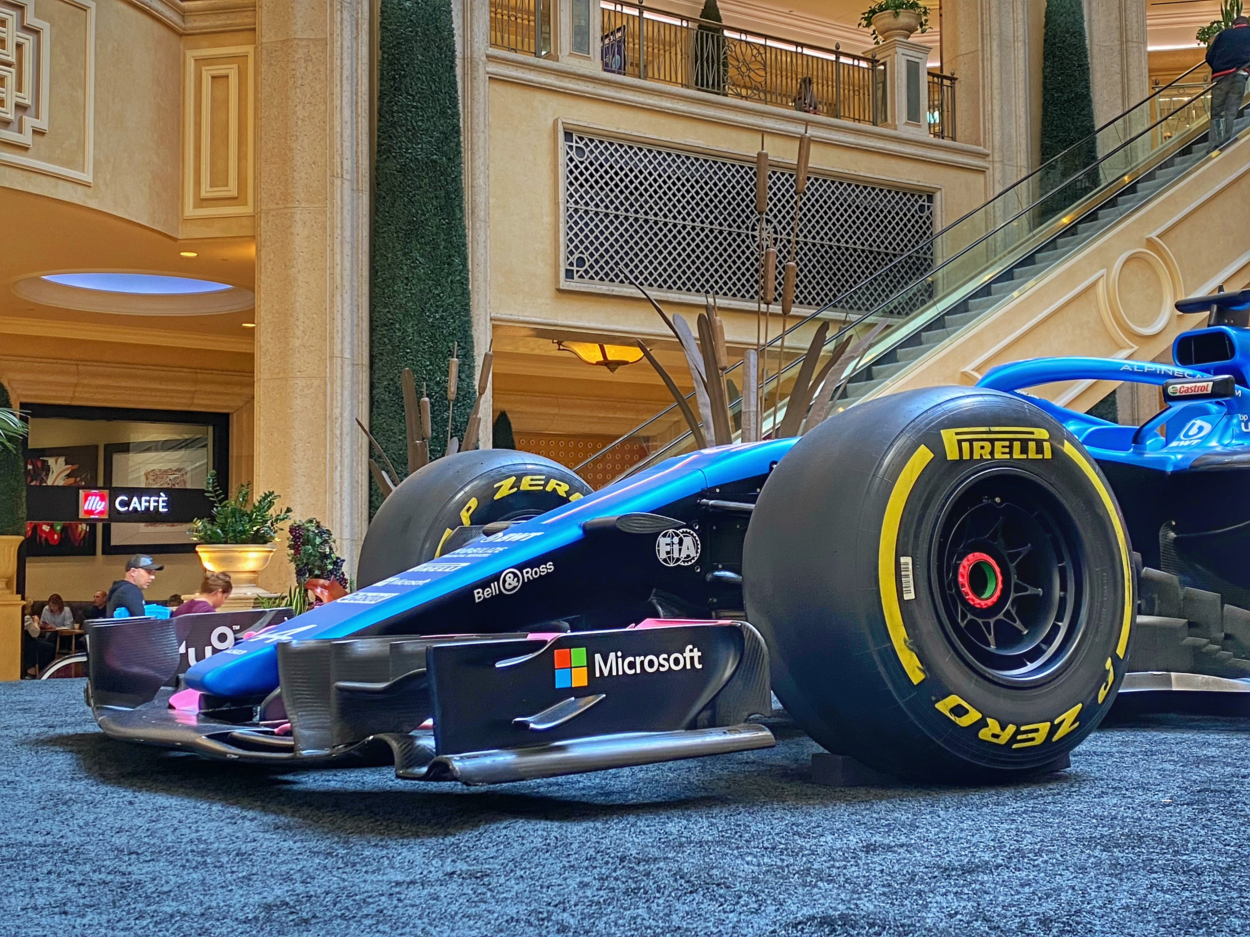 Alpine Formula 1 race car with Microsoft, Castrol, and Pirelli branding on display inside a luxury shopping mall near illy Café