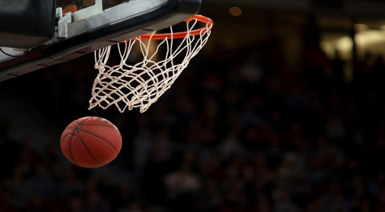 Close-up of a basketball going through the net during a game with blurred crowd in the background