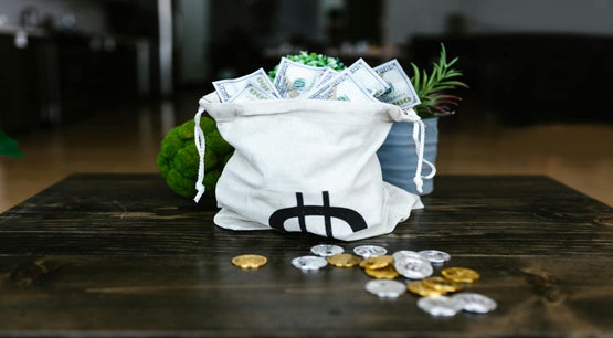 Money Bag with Cash and Coins Representing Wealth and Finance Cloth money bag filled with US dollar bills and surrounded by gold and silver coins on a table