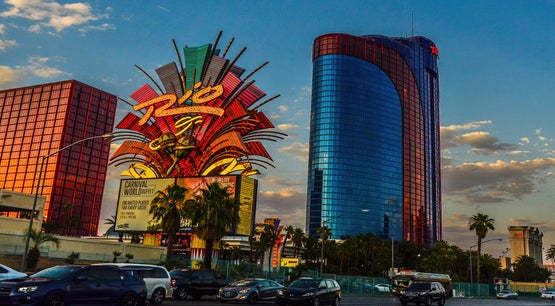 Exterior view of the Rio Hotel & Casino in Las Vegas, featuring the resort's iconic neon sign and blue glass tower